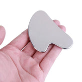 Heart shaped stainless steel gua sha facial sculpting tool being held in a hand GlowNest Co